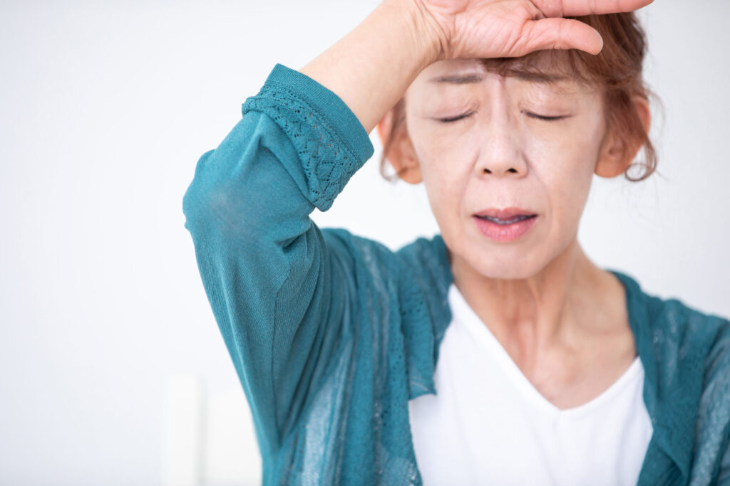 更年期の不調で朝から肩や背中の重だるさを感じ、疲れが抜けずにつらそうにしている女性の表情
