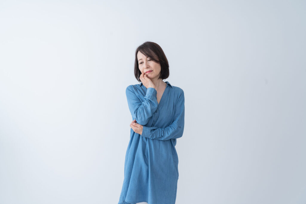 更年期の不調に悩む中年女性が考え込む様子。肩こりや腰痛、自律神経の乱れを抱えた表情。