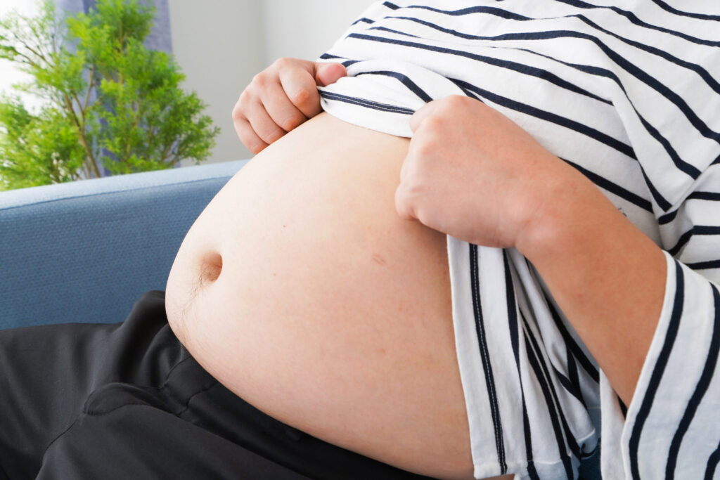 お腹の張りを感じてシャツをめくる男性の様子。便秘や内臓不調などの体のサインを示す場面。