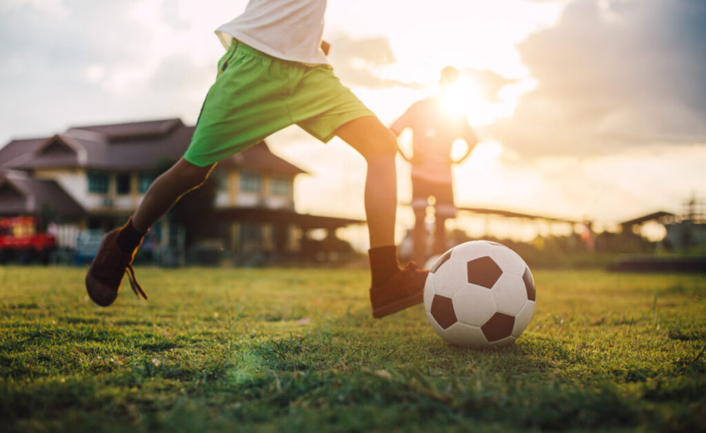 夕方のグラウンドでサッカーボールを蹴る子どもの足元