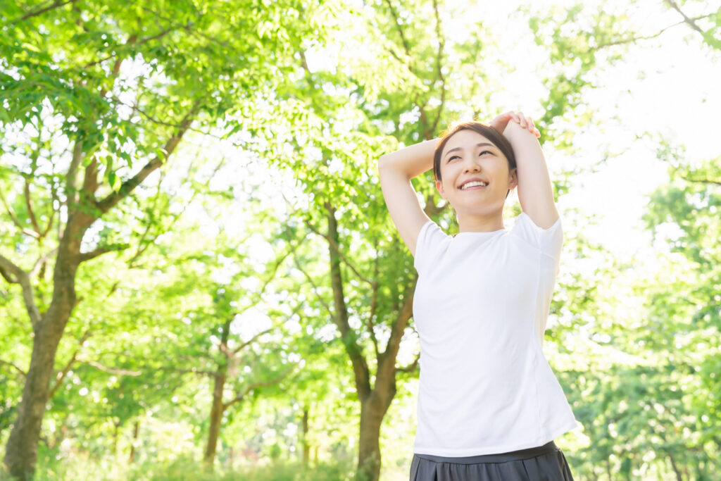 鹿児島市荒田のまどか整体院をイメージさせる、晴れた日の公園でストレッチをする女性の姿。気象に左右されない健やかな身体づくりを象徴