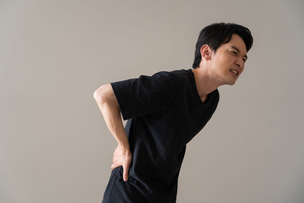 前かがみの姿勢で腰の痛みに顔をゆがめる男性。鹿児島市のまどか整体院では、脊柱管狭窄症による腰痛や脚のしびれの根本改善をサポートしています