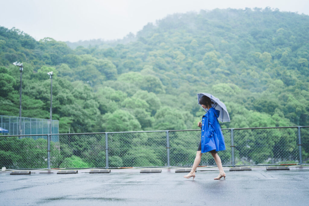 梅雨の雨の中を傘をさして歩く女性。湿度の高い時期の不調や気象病を連想させる風景