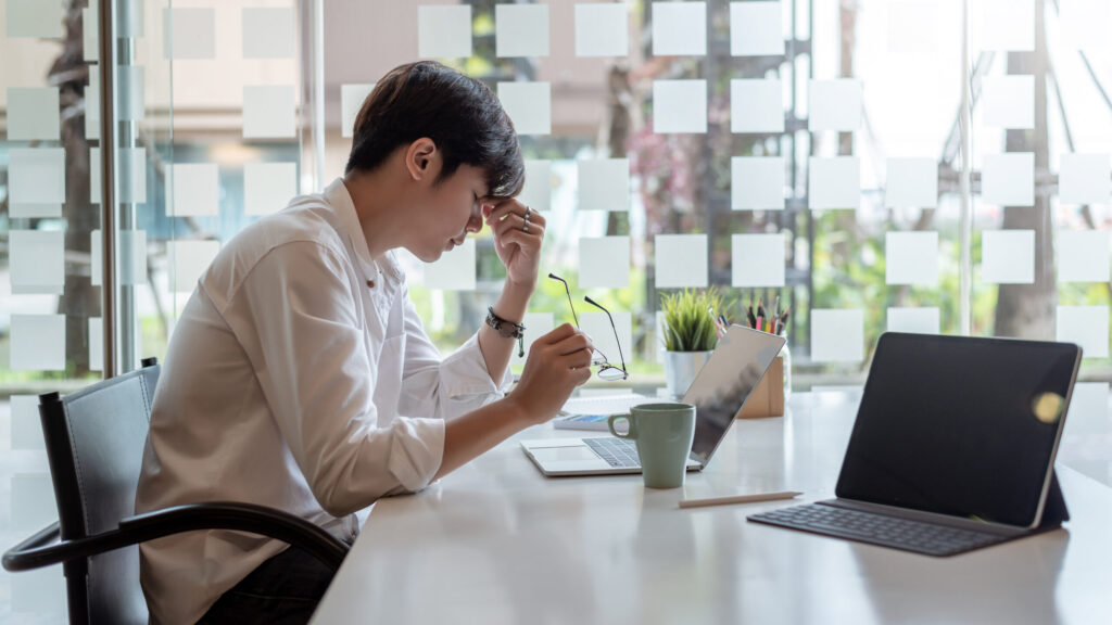 パソコン作業中に目を押さえる男性。鹿児島市のまどか整体院では、スマホやPCの使いすぎによる首・目の不調“現代型不調”にも対応しています
