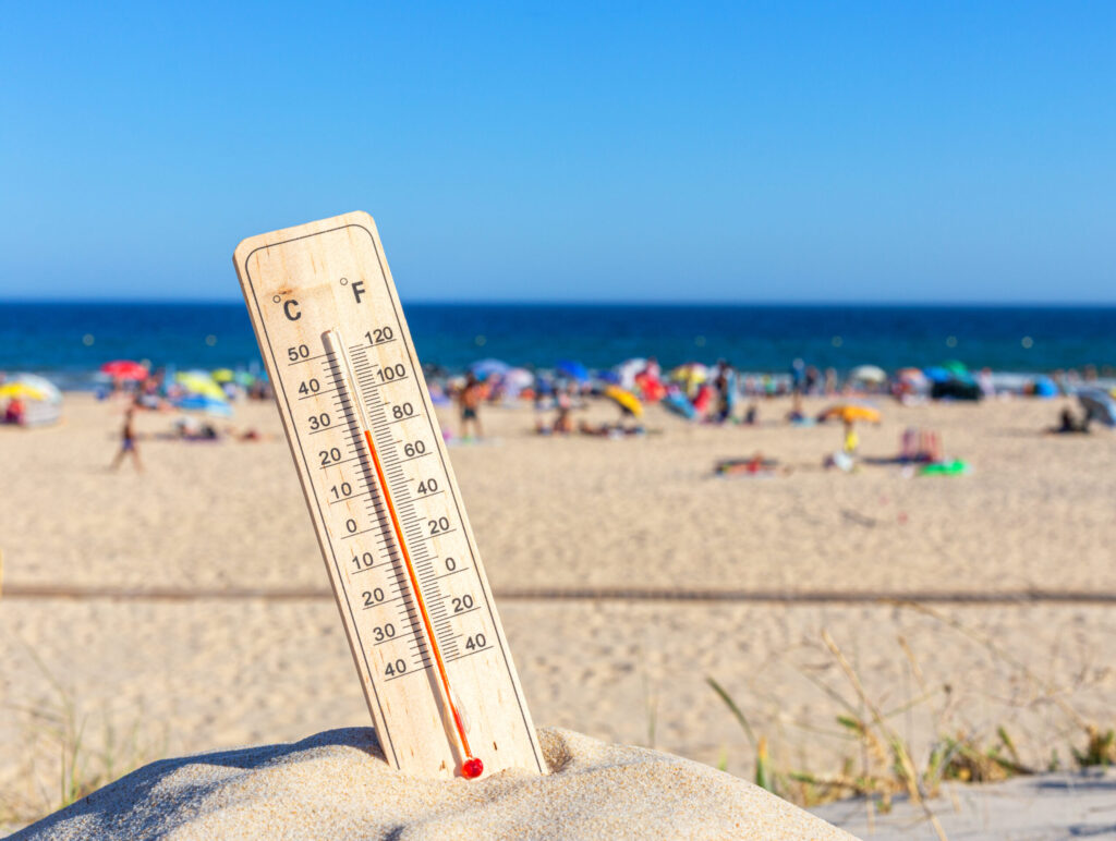 真夏の海辺に立てられた温度計と暑さでにぎわうビーチの風景