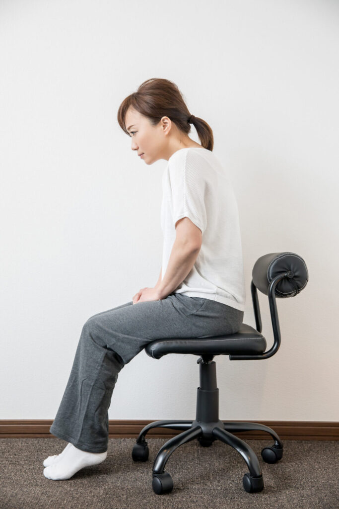 椅子に座って猫背の姿勢になっている女性。姿勢の崩れが肩や腰の不調につながることを示すイメージ【鹿児島まどか整体院】