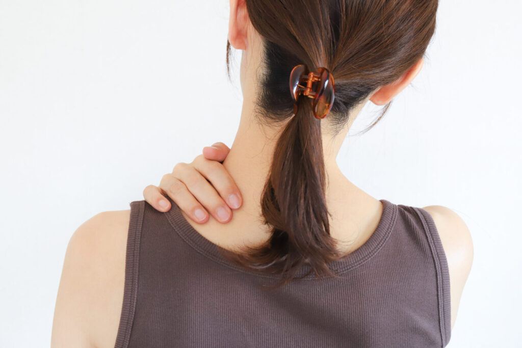 肩こりに悩む女性が首から肩を押さえている様子