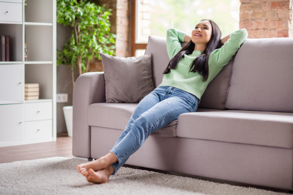 ソファに深く腰かけてリラックスする女性。姿勢を崩してくつろぐ様子